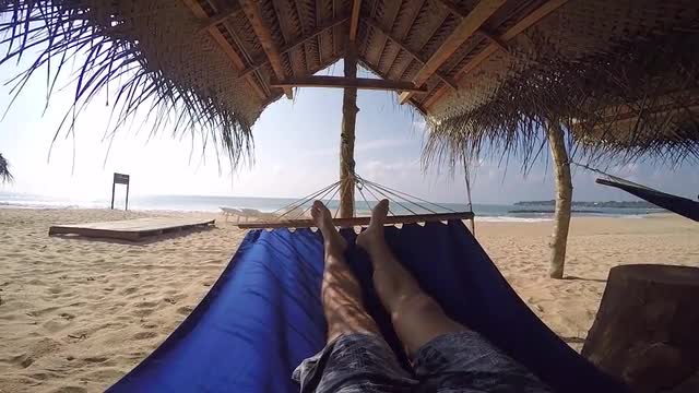 pov man in hammock in the shade of palmtrees on tropical beach