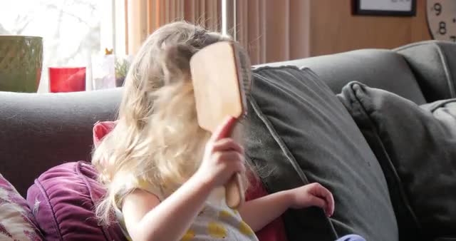 Caucasian preschooler brushing her hair on sofa