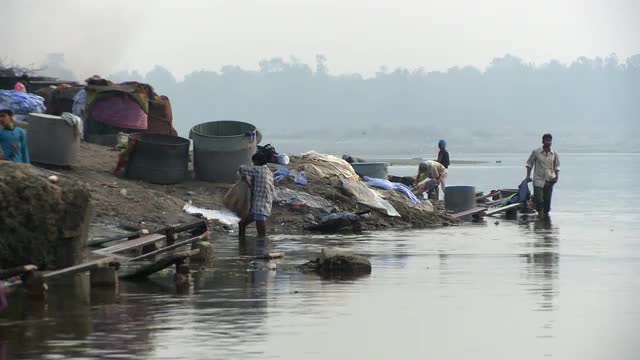 Man washing and beating clothes on board in river