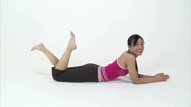 Woman laying on her stomach, kicking her feet, and smiling on a white background.