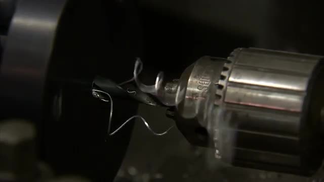 Close up of a drill that is stationary while metal spins around it.