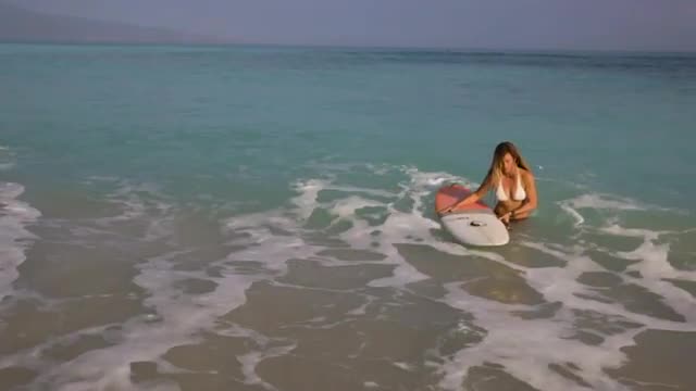 Woman padding surf board and getting out of tropical ocean in bikini
