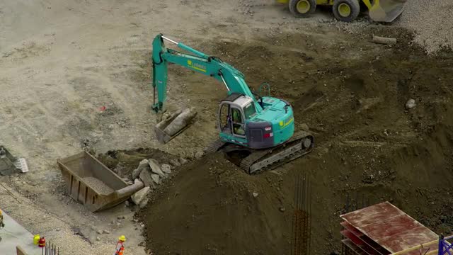 A backhoe lifts large rocks from atop a dirt pile