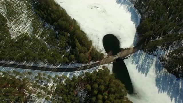 High aerial shot of a country road with melt ice around a bridge at a springtime lake