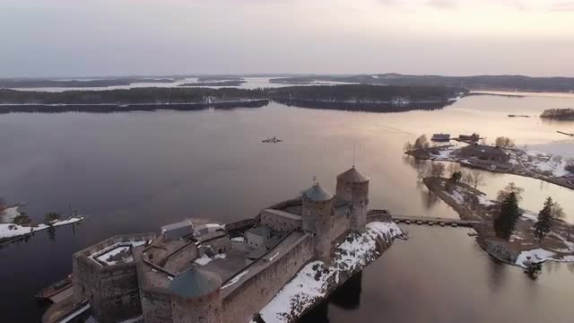 Backwards overflight aerial shot of a medieval castle in the lake landscape in Finland