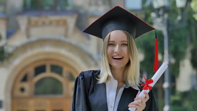Graduand in Mantle Demonstrating Her Diploma Smiling Standing in Alley Outside the Univesrsity Happy