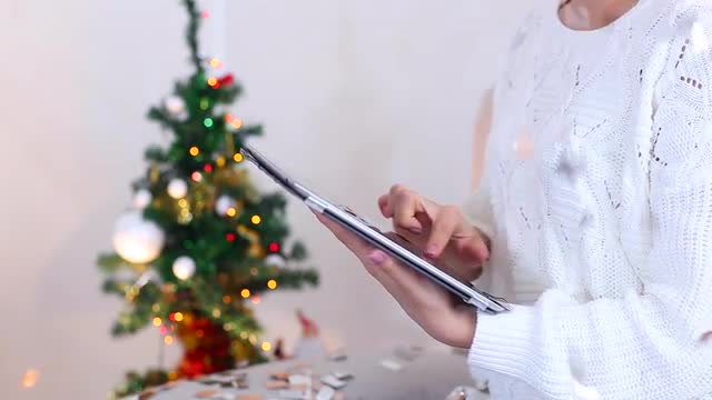 Young Girl Uses Hand Hold Press Tablet on Bokeh Xmas Eve Lights New Year Tree Confetti Christmas