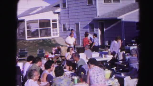 1962: a large number of people gather on a clear sunny day on benches to have eat and get together. 