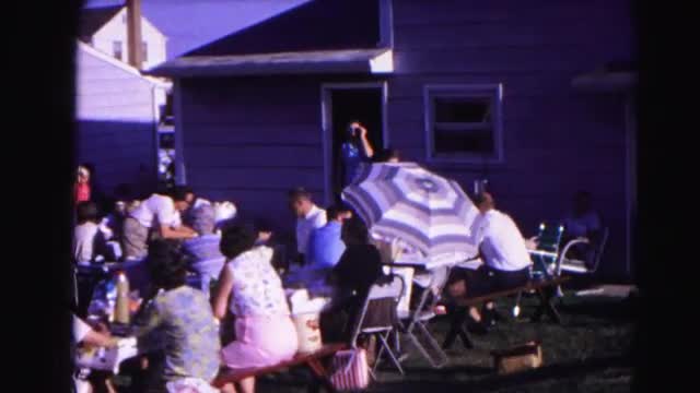 1962: a large group of people gathered on a clear and sunny day sitting on benches and picnic tables