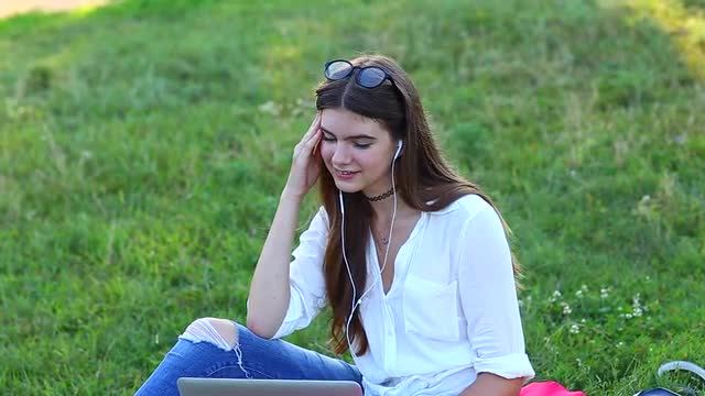 Lady Sitting in the Park and Talking on Skype Via a Laptop With Headphones