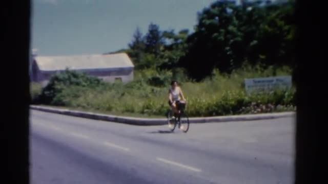 1951: a woman cautiously rides her bicycle across an intersection as a car speeds by. FLORIDA 1951: a woman cautiously rides her bicycle across an intersection as a car speeds by. FLORIDA
