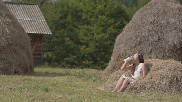 Brunette girl drinking fresh milk on meadow in the village