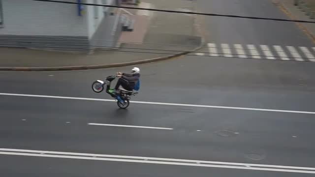 Biker rides on rear wheel of scooter on the street