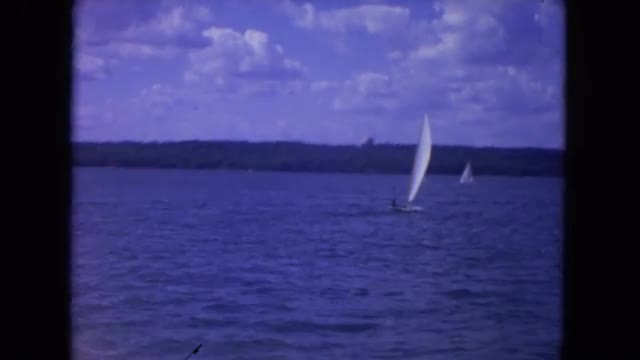 1972: view from a harbor of beautiful sailboats on the ocean with hills and trees in the distance CH