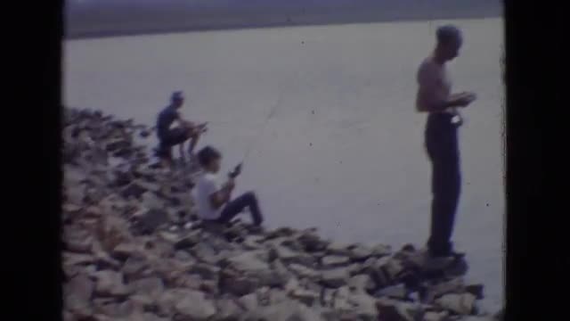 1965: men and boys fishing on a rocky shoreline with rods and bait on a cloudy day NEW JERSEY