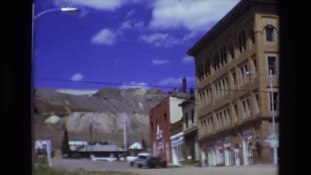 1969: empty street near a brown brick four story building that has a line wire crossing across it to