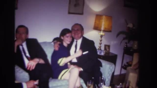 1967: friend gathered meeting hugging each other sitting sofa smoking wearing coat dress lamp on sid