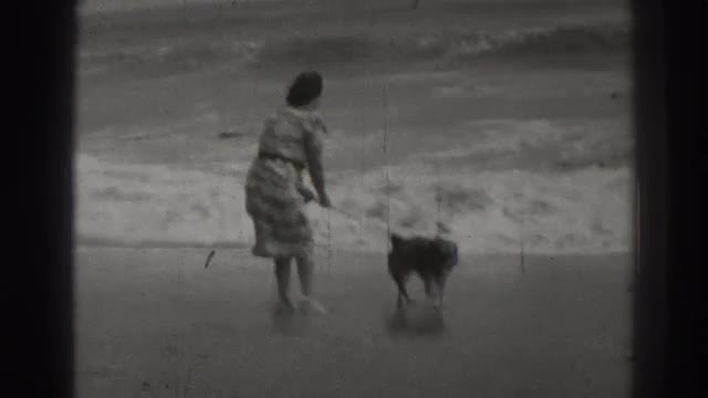 1937: lady playing in the beach with dog SANTA CRUZ CALIFORNIA
