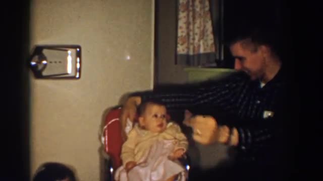 1958: a baby sitting in a red chair wearing a yellow sweater and white dress ALIQUIPPA, PENNSYLVANIA
