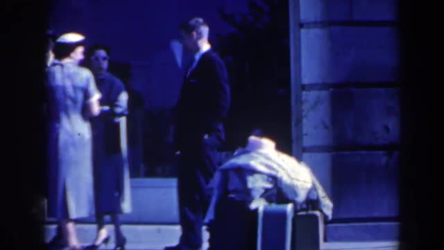 1963: a gentleman in formal suit standing near to some luggage and wishing NIAGARA FALLS