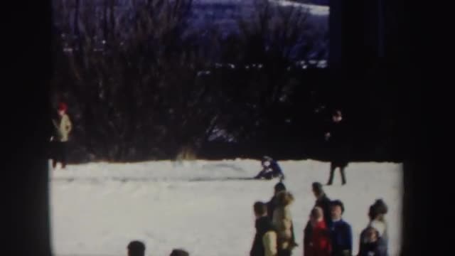 1962: spectators line a landing area while a ski competitor lands a fairly easy jump, falling at the