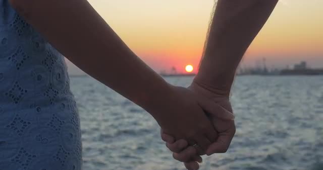 Close-up shot of romantic couple holding hands on the beach against sunset Piraeus, Greece