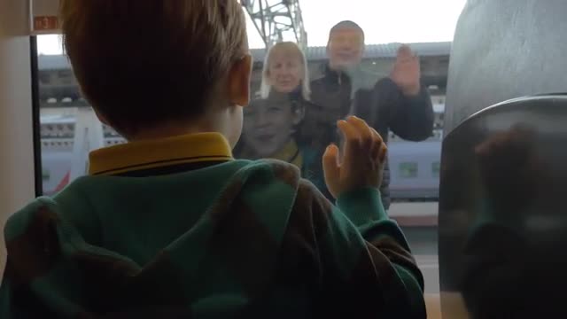 Back view of boy watching in window from rail train and saying goodbye his grandparents, swinging ar