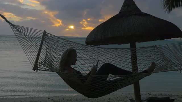 Woman with phone lying in hammock on the beach