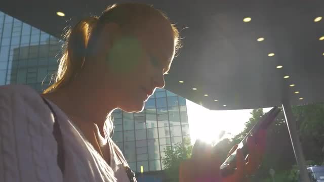 Woman with cell in city against bright sunshine