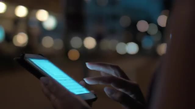 Woman typing on cellphone walking in night city