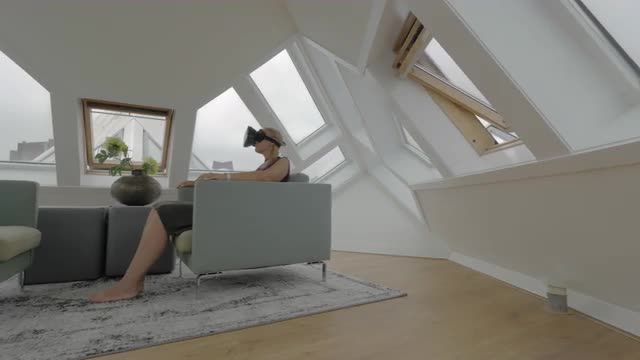 View of young blond woman sitting on the side of arm chairs using tablet inside of room in a Cube ho