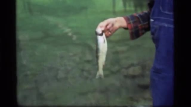 1977: man standing by lake holding a trout by the gills SAPPHIRE LAKE MONTANA