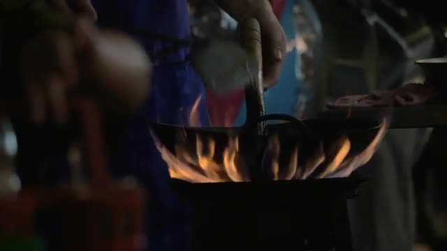 Man cooking noodle dish in wok on open fire, Thailand