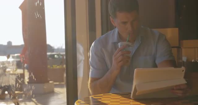 Young man searching something in tablet drinking iced tea from tubule