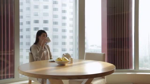 MS PAN Woman drinking tea at table in front of window / China