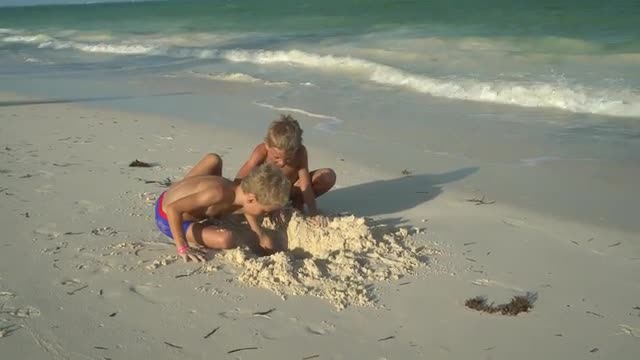 two boys digging a hole in sand on beach
