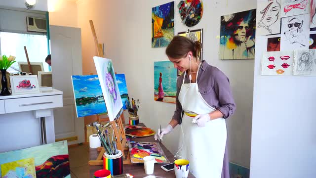 Charming Artist Draws Picture Uses Brushes With Oil and Listening Music on Headphones Through Phone,