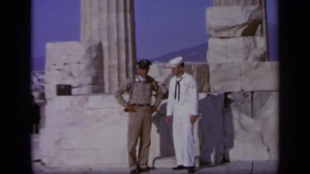 1963: soldier and sailor pose together by rigid columns and stone blocks GREECE