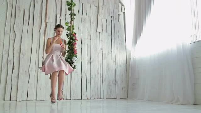 2 shots. Woman with make-up on a swing decorated with flowers blowing bubbles 2 shots. Woman with make-up on a swing decorated with flowers blowing bubbles