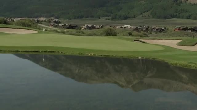 Medium shot of golfer hitting chip shot over pond onto green