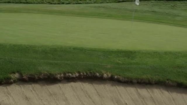 Medium close up of golfer hitting bunker shot onto green