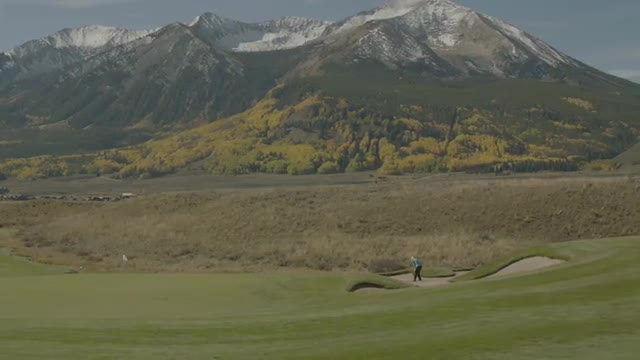 Wide shot of golfer hitting bunker shot next to golf green