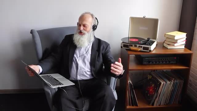 Pensioner at Top of Voice and With Emotions Sings Favorite Hits, Sitting in Chair With Laptop in Hea