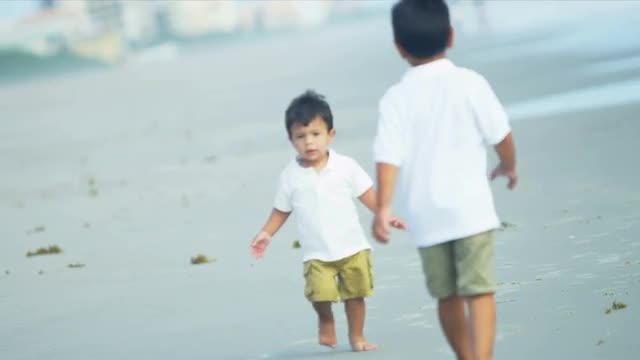 Happy Hispanic brothers walking together on beach 