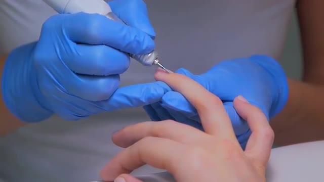 Hardware manicure in a salon. Manicurist is applying electric nail file drill