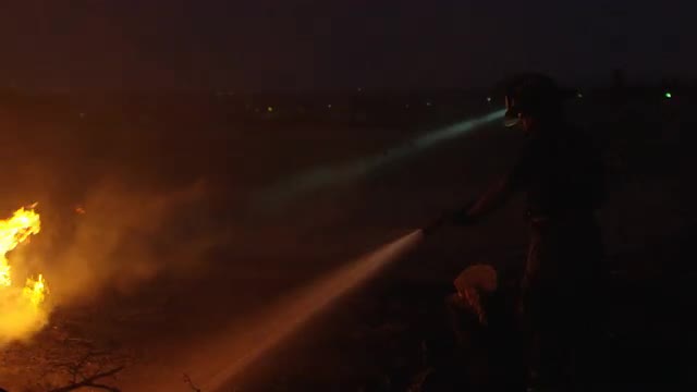 Fireman spraying water on fire after dark