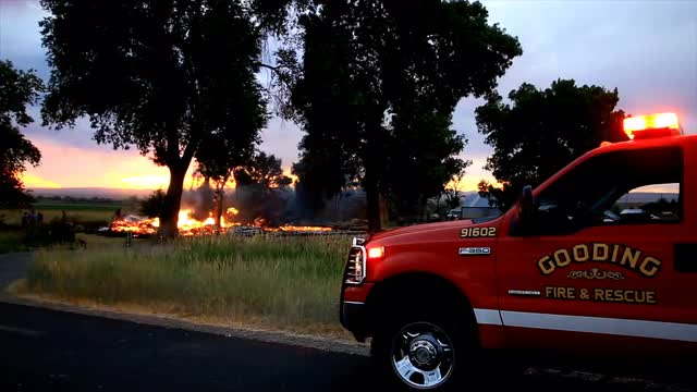 Fire department truck with lights flashing as house fire is in the background.
