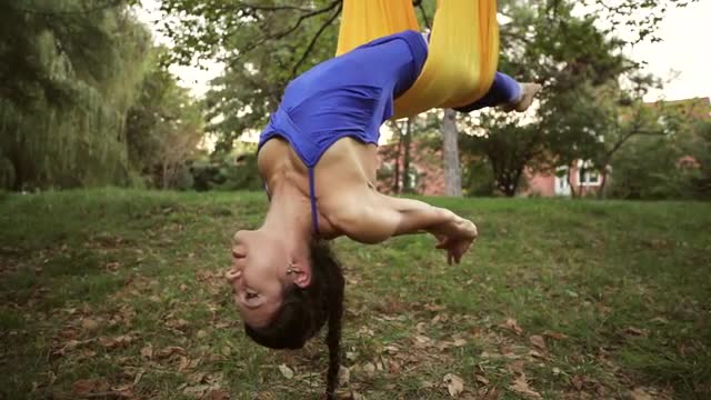 Aerial yoga practitioner stretches herself while suspended on hammock.
