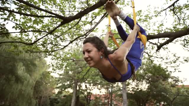 Aerial yoga practitioner stretches herself while suspended on hammock.