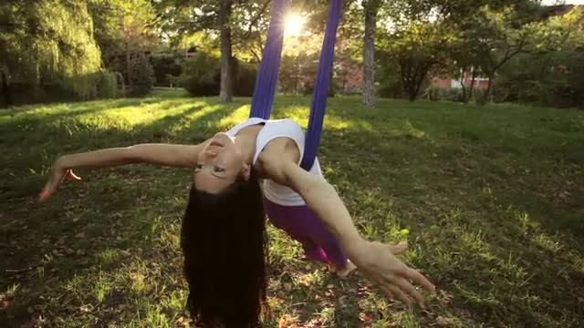 Aerial yoga practitioner stretches herself while suspended on hammock.